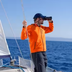 Entrepreneur sur un bateau utilisant des jumelles pour chercher un logiciel comptable adapté, symbolisant la recherche d’un expert-comptable Pennylane Nantes.
