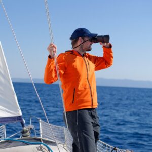 Entrepreneur sur un bateau utilisant des jumelles pour chercher un logiciel comptable adapté, symbolisant la recherche d’un expert-comptable Pennylane Nantes.