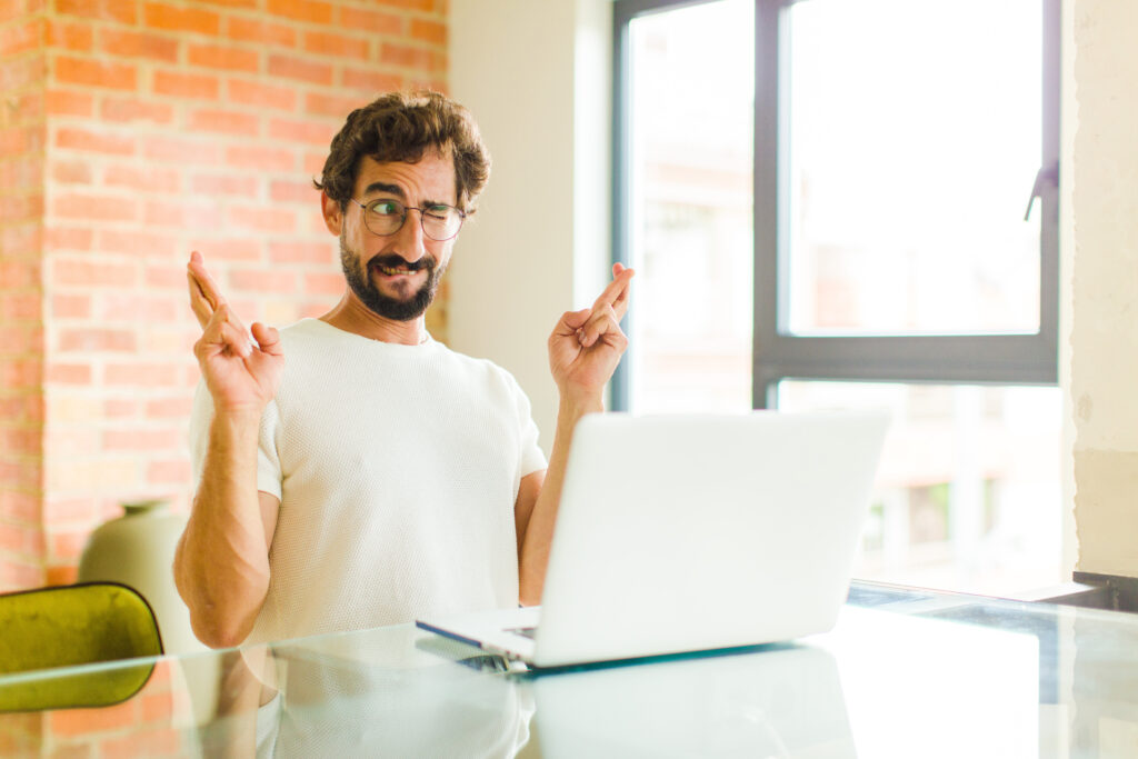Entrepreneur devant son ordinateur, les doigts croisés et les yeux fermés, espérant une transition réussie vers Pennylane avec son expert-comptable Nantes.